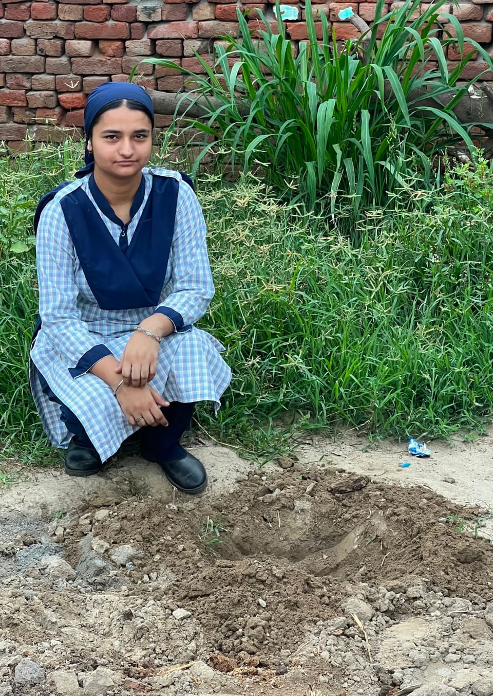 A student kneeling beside a freshly dug planting pit