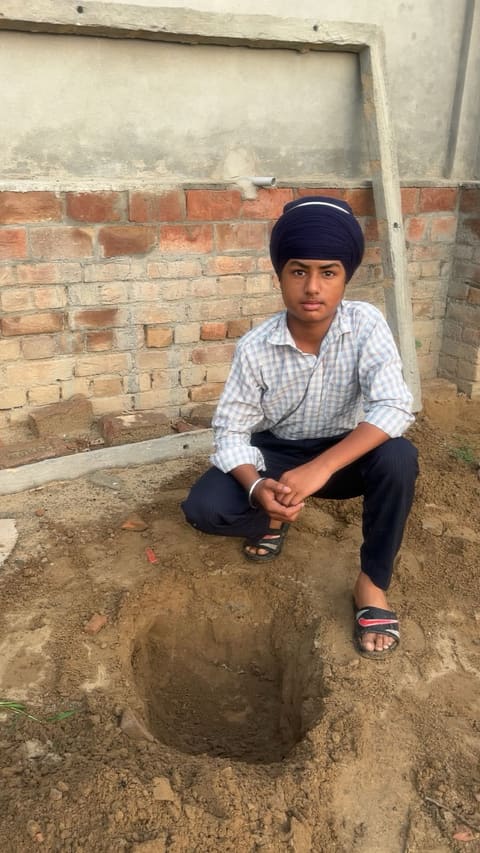 A student sitting beside a planting pit ready for a sapling