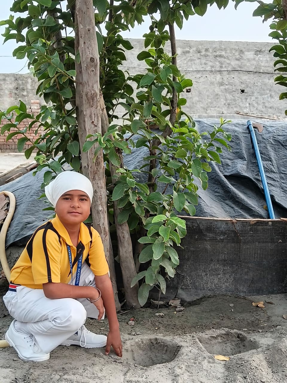 A student kneeling beside a young tree during the plantation drive