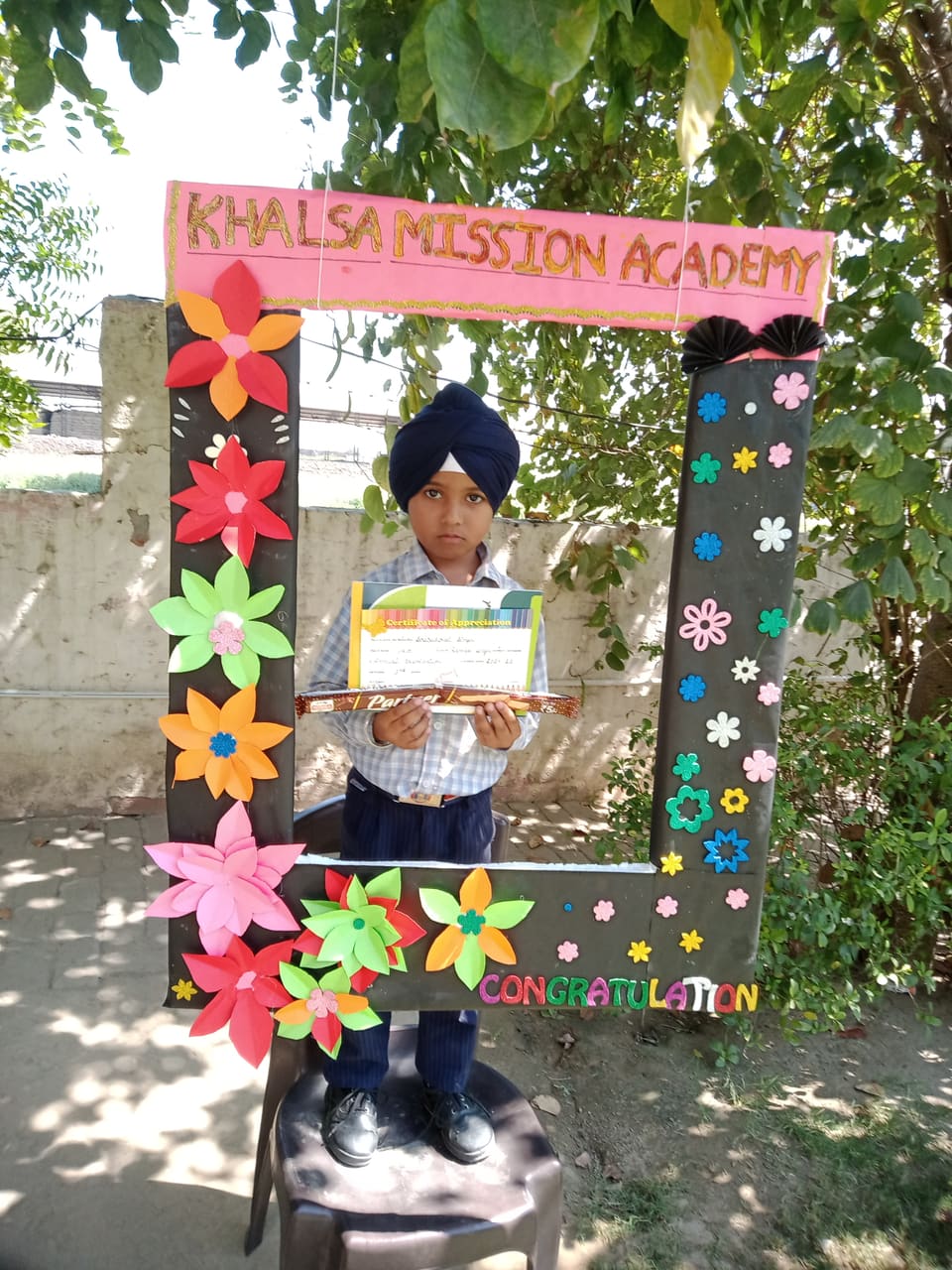A student holding a certificate beside a decorated congratulations board