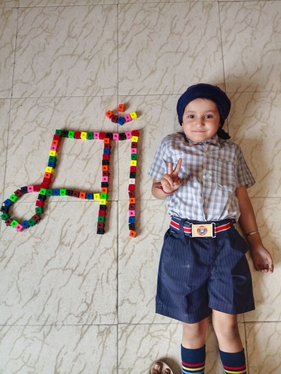 A young student beside a Punjabi letter built from coloured blocks