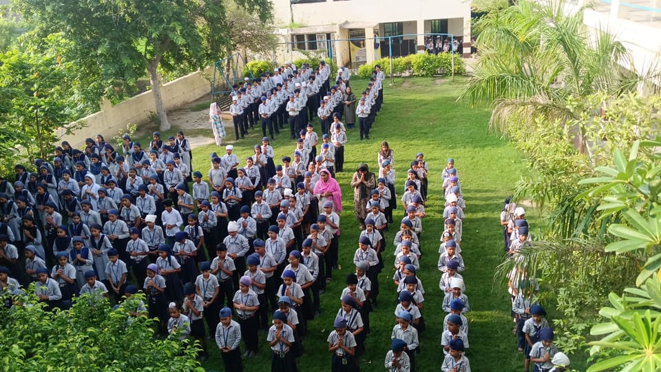 Students in neat rows on the green lawn with the school building behind