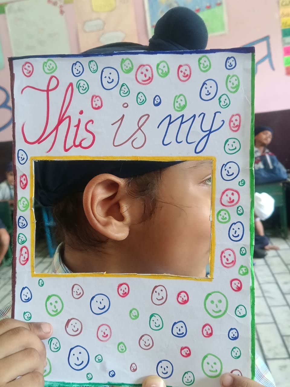 A child holding a hand-decorated frame around their ear for a senses lesson
