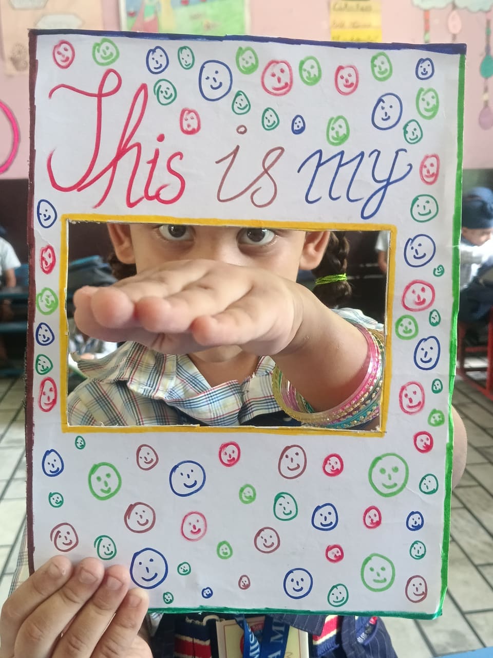 A child holding a decorated craft frame around their hand