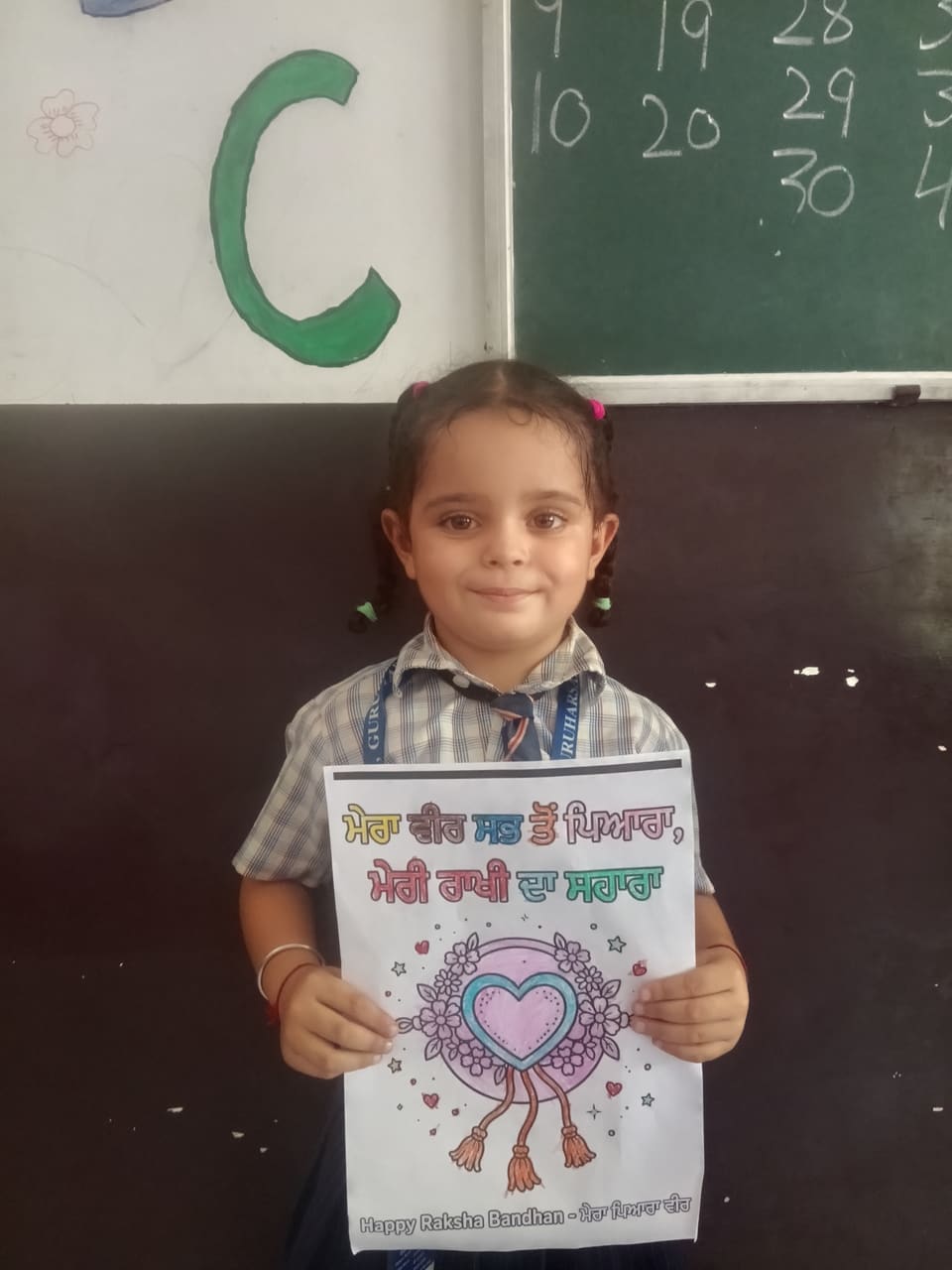 A young student holding up her coloured Rakhi drawing