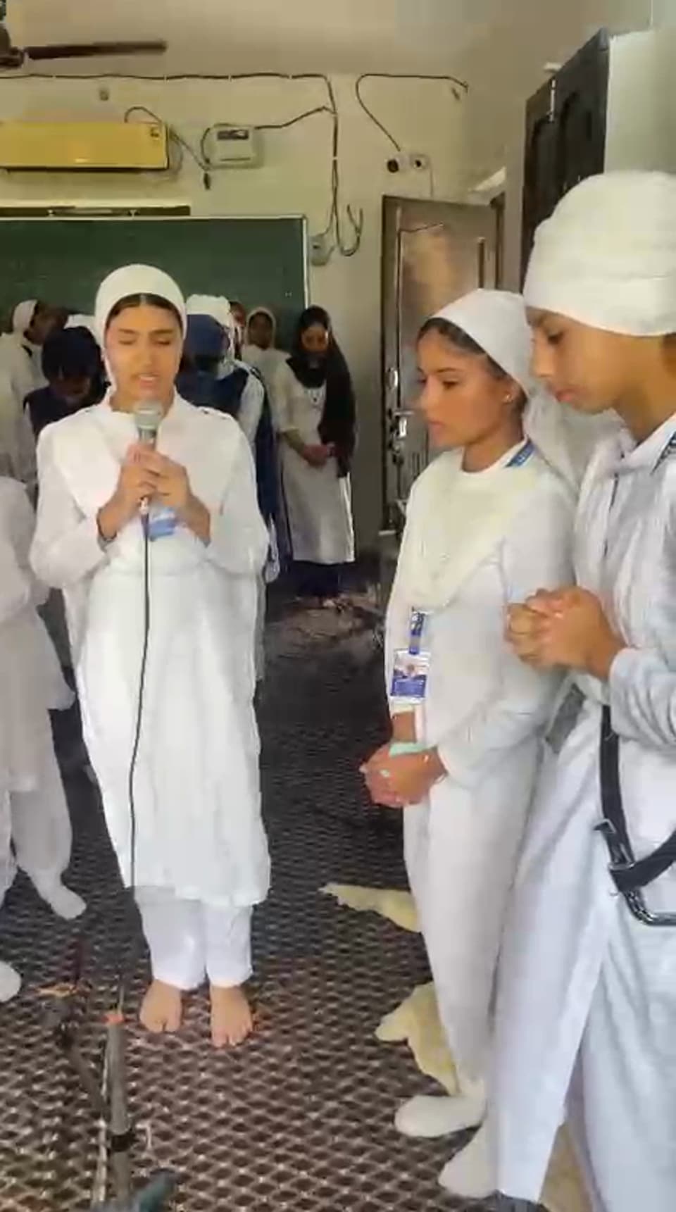 Students in white singing shabad kirtan at the microphone